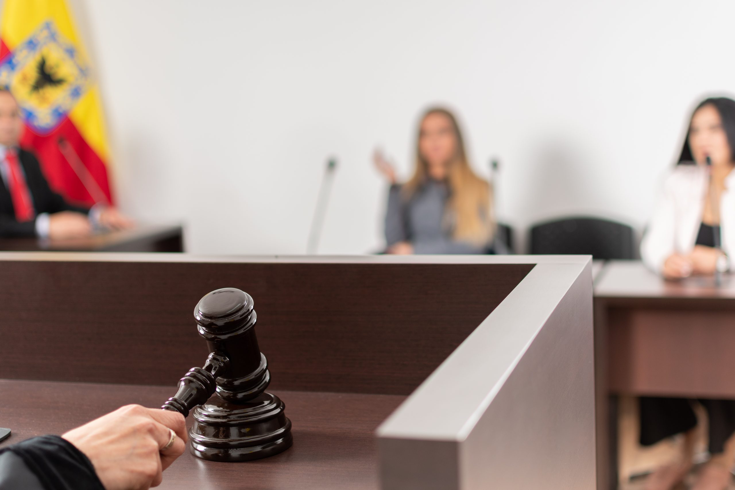 Close-up of a gavel on a judge's bench in a courtroom setting, with blurred figures of a lawyer and two women in the background, emphasizing legal proceedings related to DUI cases.