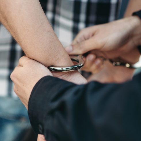 Police officer puts handcuffs on a car thief, policeman arrests the driver violator on road. Cop at the work. Law protection concept, professional safety control