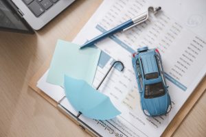 Car insurance protect safe transport. Safety trust. Protection secure assurance. A blue car is placed on top of a clipboard with a piece of paper underneath it.