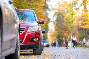 Cars parked in a row on a city street side on bright autumn day.