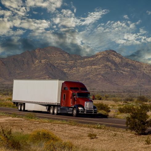 Classic big rig heavy duty long haul diesel semi truck with refrigerator semi trailer running on the road along mountains in USA