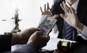 Two people in business suits are at a desk. One hands over a stack of U.S. dollars, while the other raises hands in refusal.
